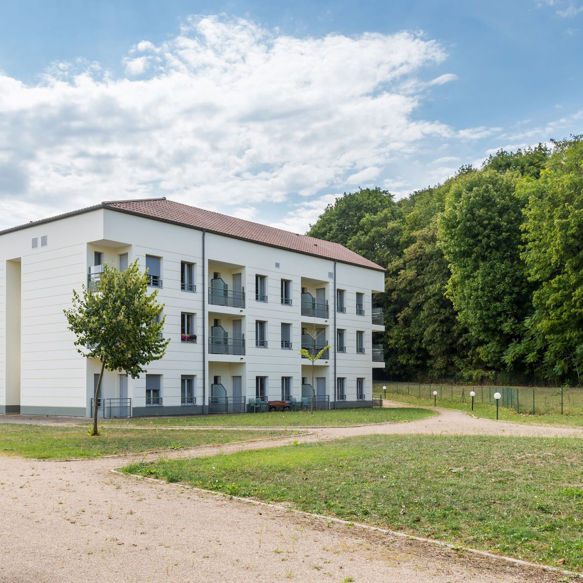 immeuble-blanc-de-trois-etages-avec-balcons-devant-un-parc-et-des-arbres